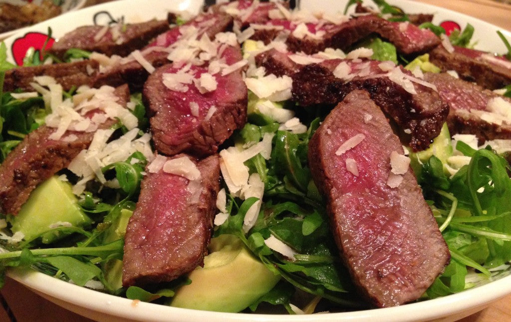 A juicy steak on a bed of arugula with creamy avocado and Parmesan
