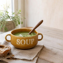 Okergele Soup soepkom met erwtensoep en houten lepel op een linnen servet