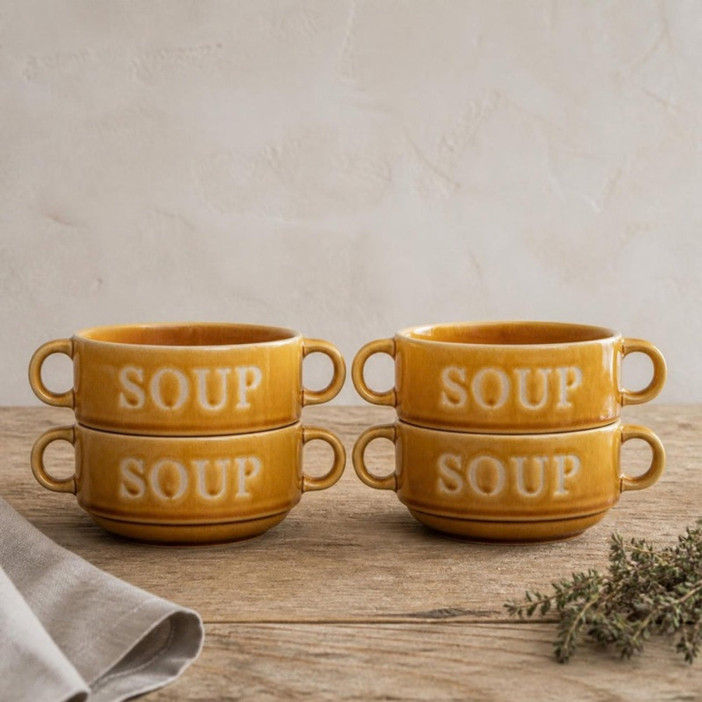 Vier okergele Soup soepkommen gestapeld in twee stapels op een eiken tafel