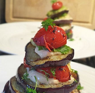 A colorful stack of grilled eggplant with avocado, hummus and cherry tomatoes